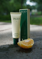 Palio sunscreen tube and packaging with an orange on a concrete surface.