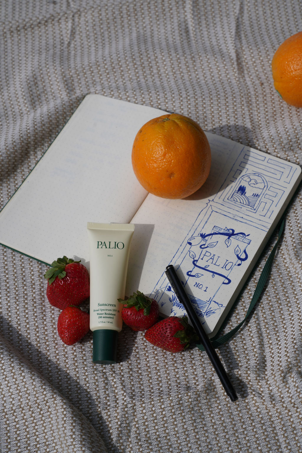 Tube of Palio sunscreen with strawberries and an orange on a textured surface