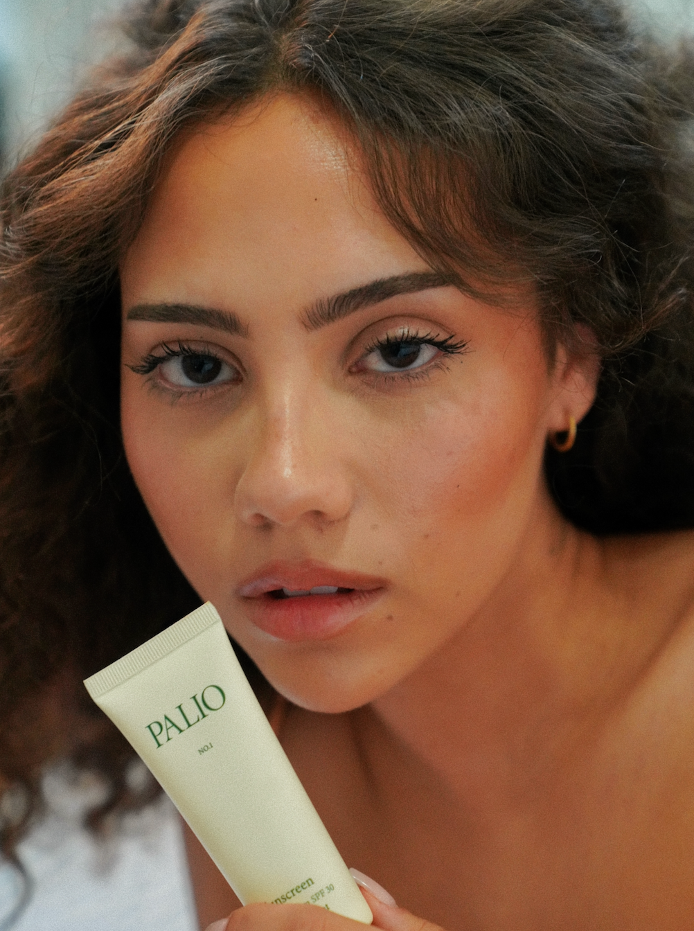 Woman holding a tube of Palio sunscreen with a blurred background