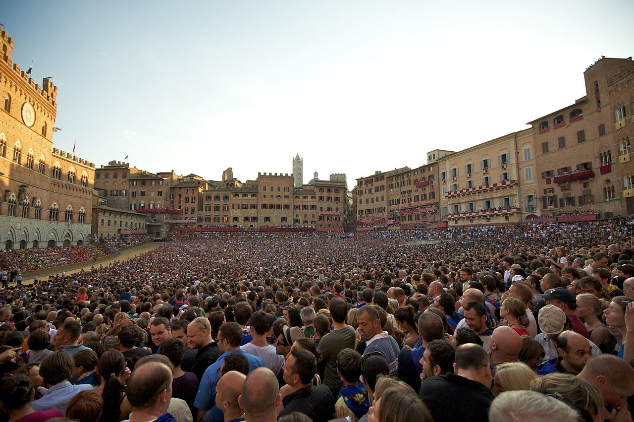 Large crowd gathered in a historic square with old buildings.